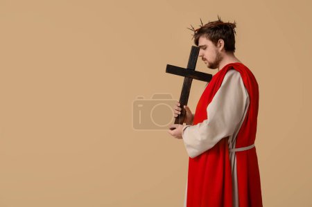 Man in Jesus robe and crown of thorns with wooden cross on beige background