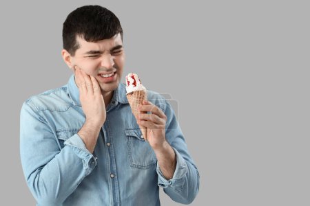Young man with ice cream suffering from toothache on light background