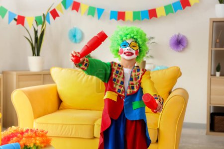 Funny little boy in clown costume with juggling clubs at home. April Fools' Day celebration