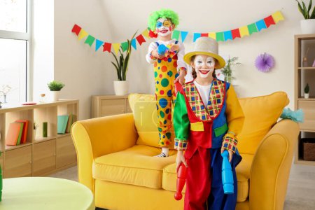 Foto de Niños divertidos con disfraces de payaso haciendo malabares en casa. Celebración del Día de los Inocentes - Imagen libre de derechos