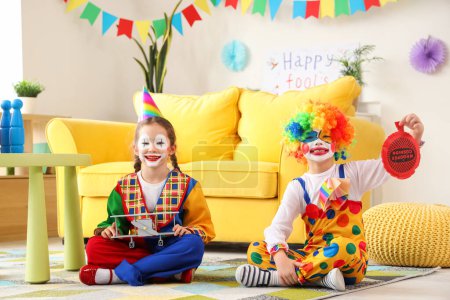 Lustige kleine Kinder in Clownskostümen mit Kissen zu Hause. Feier zum Aprilscherz