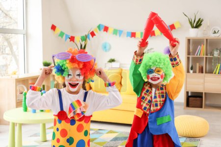 Funny little children in clown costumes with juggling clubs at home. April Fools' Day celebration