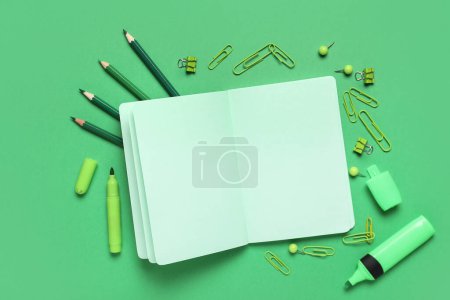 Open notebook with different stationery on green background. End of school. Top view