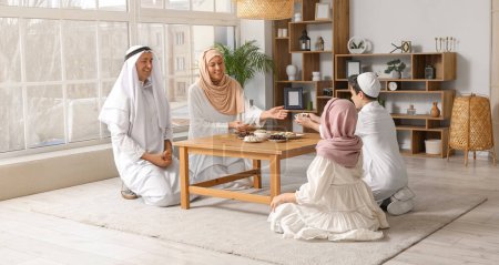 Glückliche muslimische Familie isst Süßigkeiten im Wohnzimmer