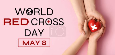 Hands of woman and child with heart on pink background, top view. Banner for World Red Cross Day