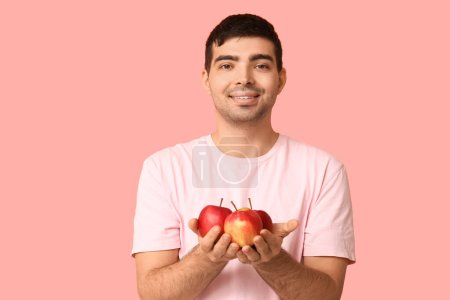 Young man with apples rich in vitamin A on pink background