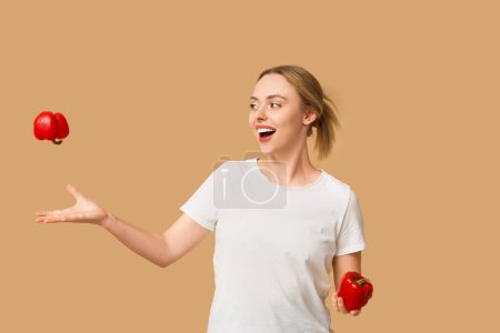 Young woman with bell peppers on beige background