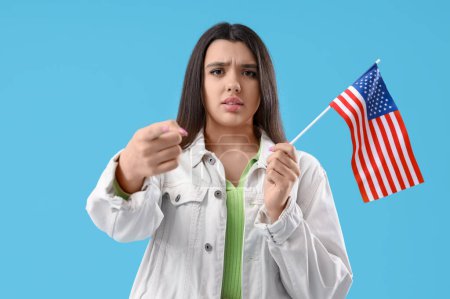 Young woman with USA flag pointing at viewer on blue background. Accusation concept