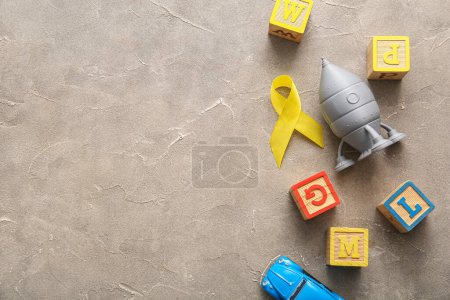 Téléchargez les photos : Ruban doré avec des jouets sur fond gris grunge. Concept de sensibilisation au cancer chez les enfants - en image libre de droit