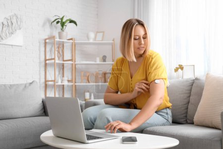 Diabetic woman with glucose sensor using laptop for measuring blood sugar level at home