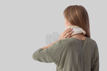Injured young woman with cervical collar after accident on light background, back view