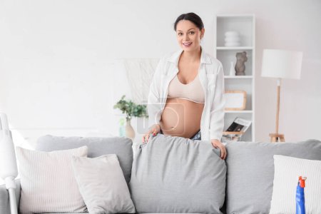 Photo for Young pregnant woman fluffing cushion at home - Royalty Free Image