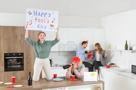 Foto de Gente de negocios con cartel celebrando el Día de los Inocentes en la cocina en la fiesta de oficina - Imagen libre de derechos