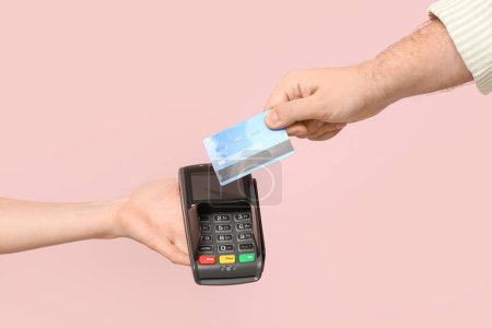 Male hand with credit card and payment terminal on pink background