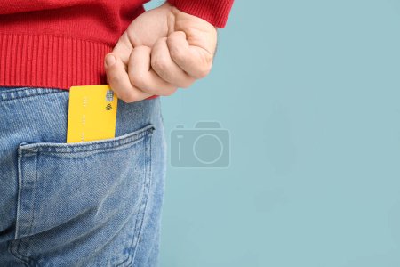 Junger Mann steckt Kreditkarte in Jeanstasche auf blauem Hintergrund, Nahaufnahme