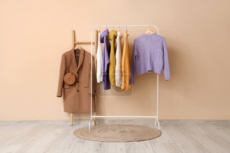 Photo for Rack of stylish clothes and rug near beige wall - Royalty Free Image