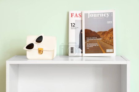 Photo for Table with magazines, stylish handbag and glasses near white wall - Royalty Free Image