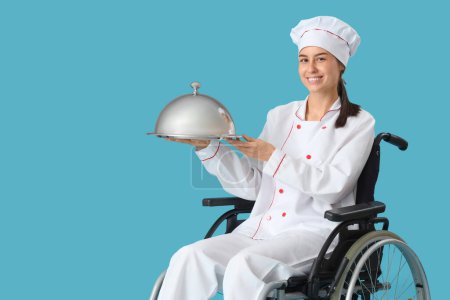 Téléchargez les photos : Femme chef en fauteuil roulant avec cloche sur fond bleu - en image libre de droit