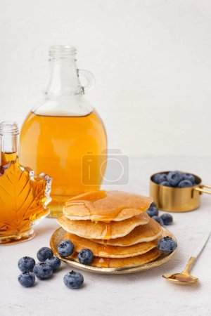 Teller mit leckeren Pfannkuchen mit Blaubeeren und Ahornsirup auf weißem Hintergrund