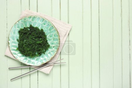 Teller mit gesunden Algen und Essstäbchen auf farbigem Holzhintergrund