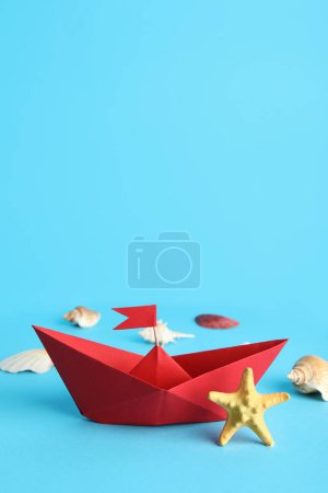 Red origami boat with seashells and starfish on blue background