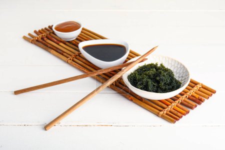 Bowls with healthy seaweed, sauces and chopsticks on light wooden background