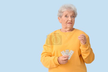 Foto de Mujer mayor conmocionada con pastillas sobre fondo azul - Imagen libre de derechos