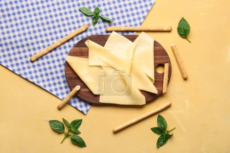 Tafel mit leckeren Käsescheiben, Basilikumblättern und italienischen Grissini auf beigem Hintergrund