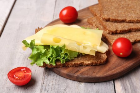 Tasty sandwich with cheese, lettuce and tomatoes on wooden background, closeup