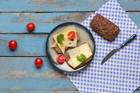 Leckere Sandwiches mit Käse, Tomaten und Petersilie im Teller auf blauem Holzhintergrund