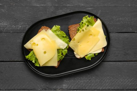 Leckere Sandwiches mit Käse und Salat auf dunklem Holzgrund
