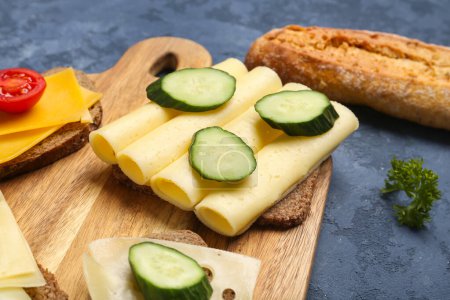 Leckeres Sandwich mit Käse und Gurke in Karton auf blauem Hintergrund, Nahaufnahme