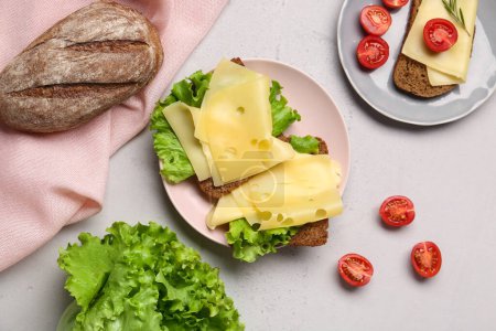 Leckere Sandwiches mit Käse, Tomaten und Salat auf hellem Hintergrund