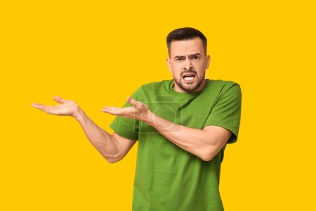 Photo for Handsome ashamed young man pointing at something on yellow background - Royalty Free Image