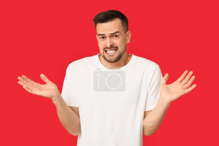 Photo for Handsome ashamed young man shrugging on red background - Royalty Free Image