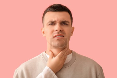 Endocrinologist examining thyroid gland of young man on pink background, closeup