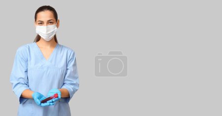 Foto de Retrato de una enfermera sosteniendo tubo de ensayo con muestra de sangre sobre fondo gris con espacio para texto - Imagen libre de derechos
