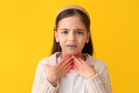 Little girl with sore throat on yellow background