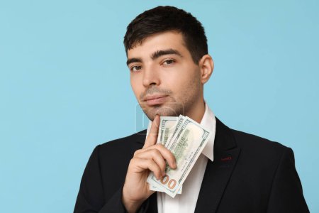 Young businessman with bribe on blue background, closeup