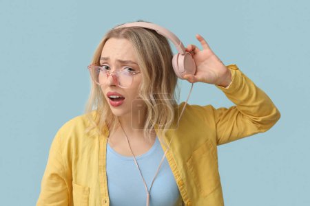 Unzufriedene junge Frau mit Kopfhörern kann nichts auf blauem Hintergrund hören