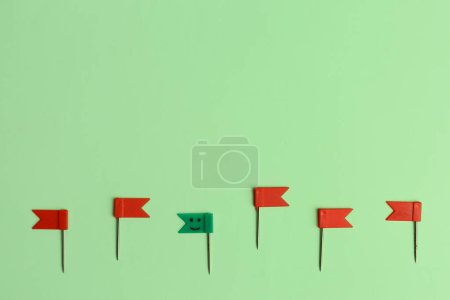 Grüne Papiernadel mit gezeichnetem glücklichen Gesicht inmitten roter auf farbigem Hintergrund. Konzept der Einzigartigkeit
