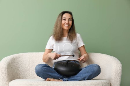 Schöne reife Frau mit Stöcken spielt glukophonisch auf dem Sofa vor grünem Hintergrund