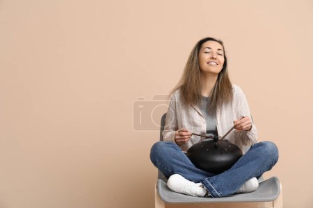 Schöne reife Frau mit Stöcken spielt glukophonisch und sitzt auf einem Stuhl vor beigem Hintergrund