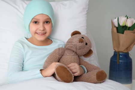 Téléchargez les photos : Petite fille après chimiothérapie avec ours jouet couché à la clinique. Journée internationale du cancer chez les enfants - en image libre de droit