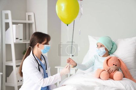 Téléchargez les photos : Petite fille après une chimiothérapie recevant un ballon bleu du médecin à la clinique. Journée internationale du cancer chez les enfants - en image libre de droit