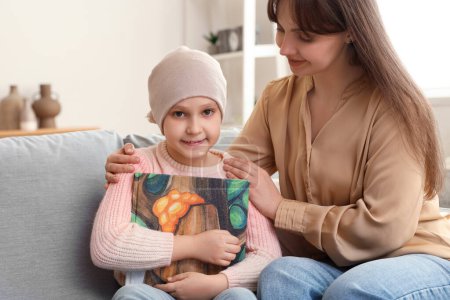 Téléchargez les photos : Petite fille après la chimiothérapie avec livre et sa mère à la maison. Journée internationale du cancer chez les enfants - en image libre de droit