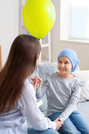 Téléchargez les photos : Petite fille après chimiothérapie avec ballon bleu et sa mère à la maison. Journée internationale du cancer chez les enfants - en image libre de droit