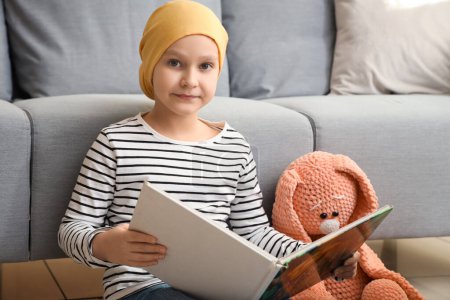 Téléchargez les photos : Petite fille après la chimiothérapie avec livre et jouet à la maison. Journée internationale du cancer chez les enfants - en image libre de droit