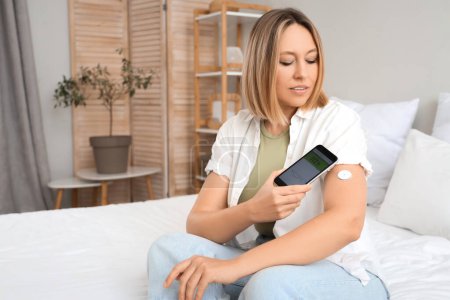 Diabetikerin mit Glukosesensor mit Handy zur Blutzuckermessung im Schlafzimmer