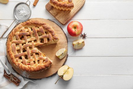 Tasty homemade apple pie with fruits, cinnamon and strainer on white wooden background